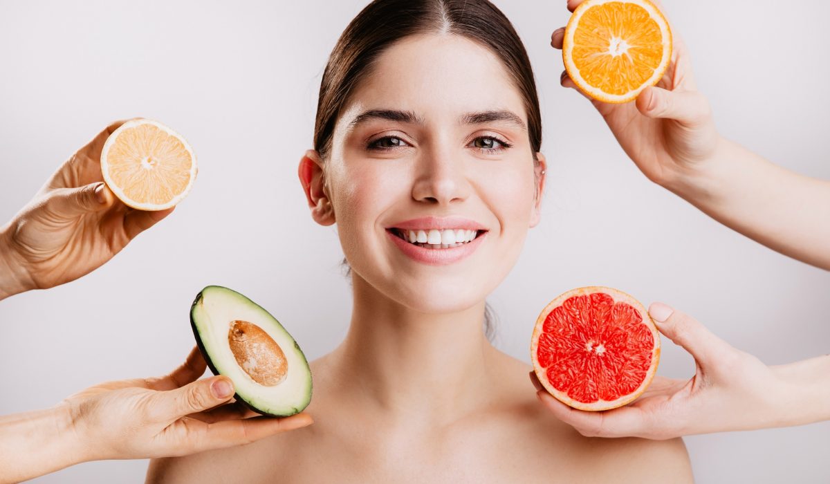 Healthy beautiful radiant skin of woman without makeup. Portrait of girl smiling against background of fruits